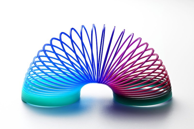 Colorful plastic spring toy in shades of blue through purple opened to form an arc on a white background