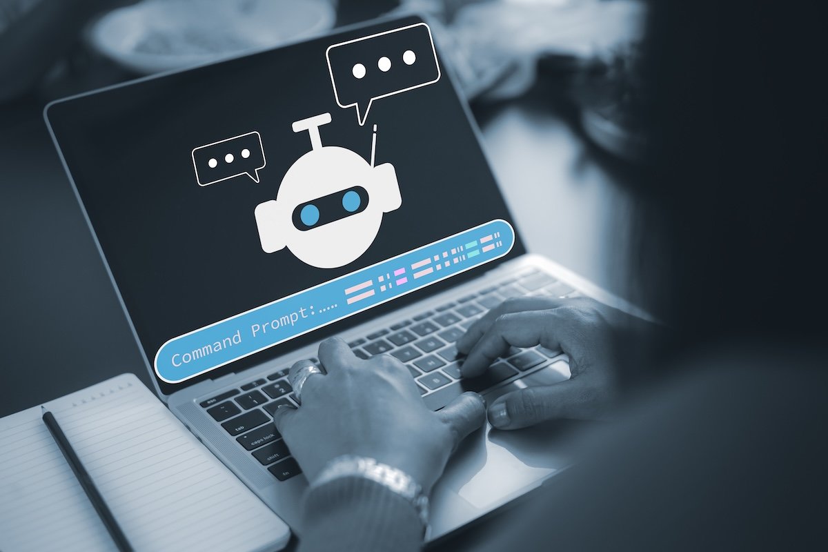 Close up of hands typing on laptop keyboard with AI chatbot icon and command prompt on screen, providing smart virtual assistant and customer support service technology concept.