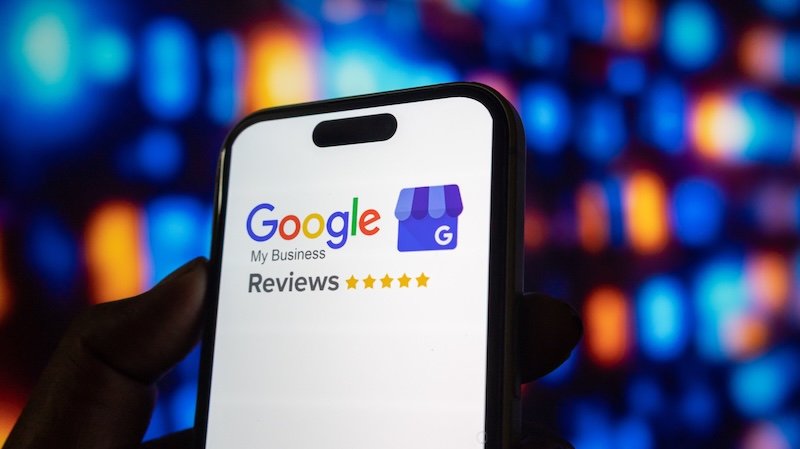 Hand holding modern smartphone screen shows Google My Business logo and star ratings. Digital technology and online reviews concept background with abstract bokeh lights.